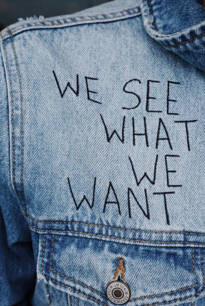 Close-up of denim jacket featuring the phrase 'We See What We Want' embroidered.